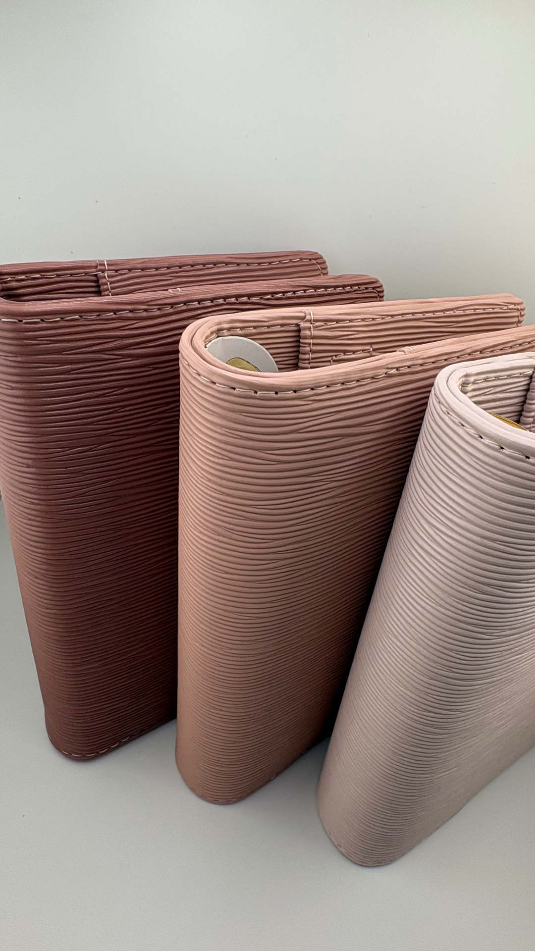 Three fine-line textured binders standing together in burgundy, rose and soft blush