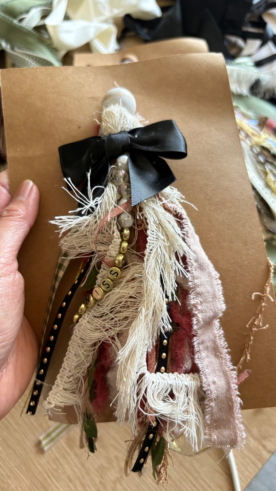 Close-up of a handmade Bible bookmark with black satin bow, gold letter beads and cream fringe on a kraft card