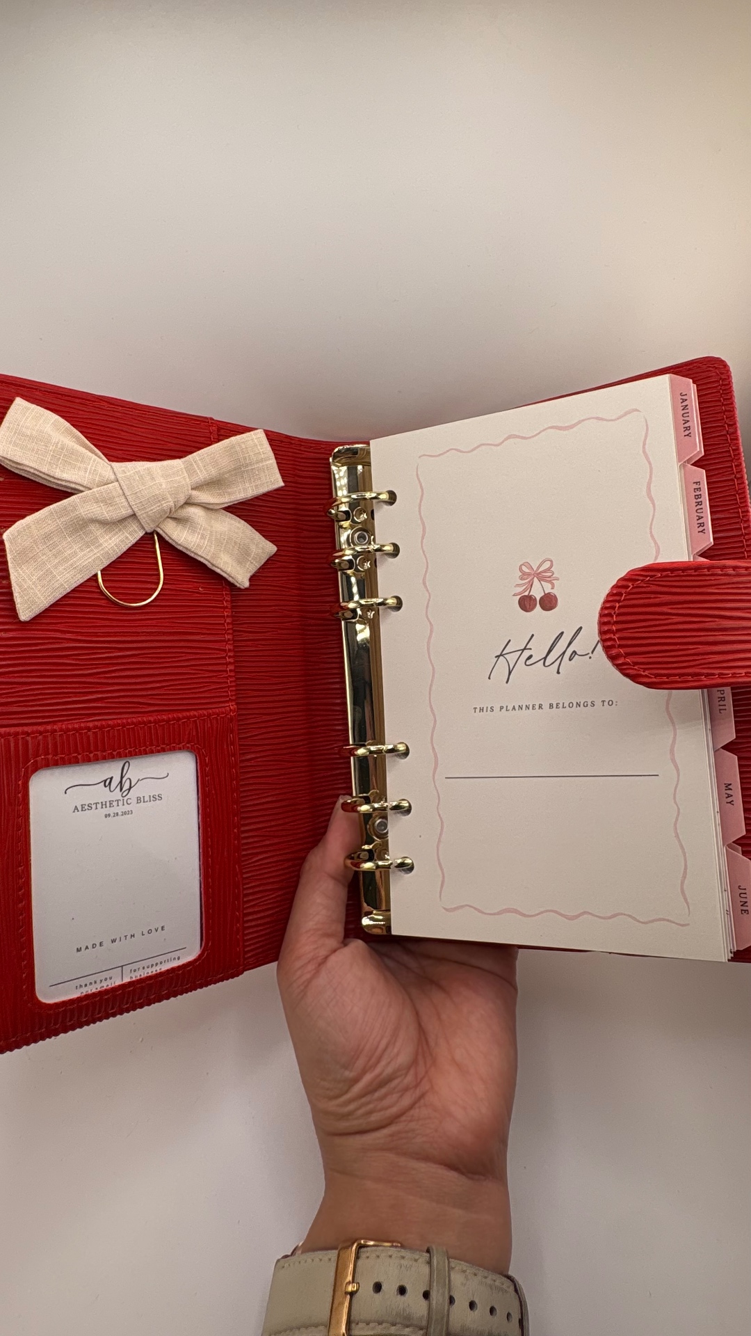 Red binder open to a hello page with cream monthly dividers and a linen bow clip